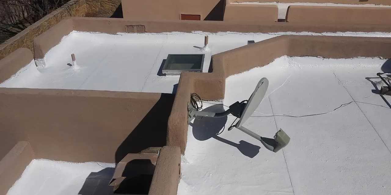 Flat roof coated white between tan stucco parapet walls, with a skylight